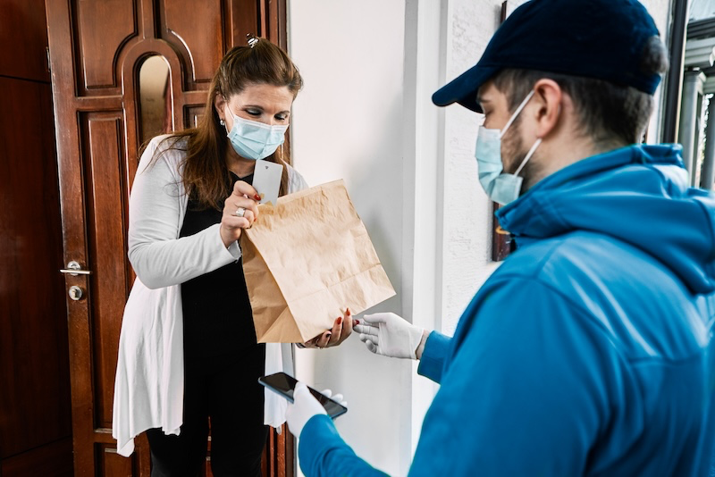 A delivery driver in uniform handing a package to a customer while holding a mobile tablet displaying a digital delivery form for signature capture.