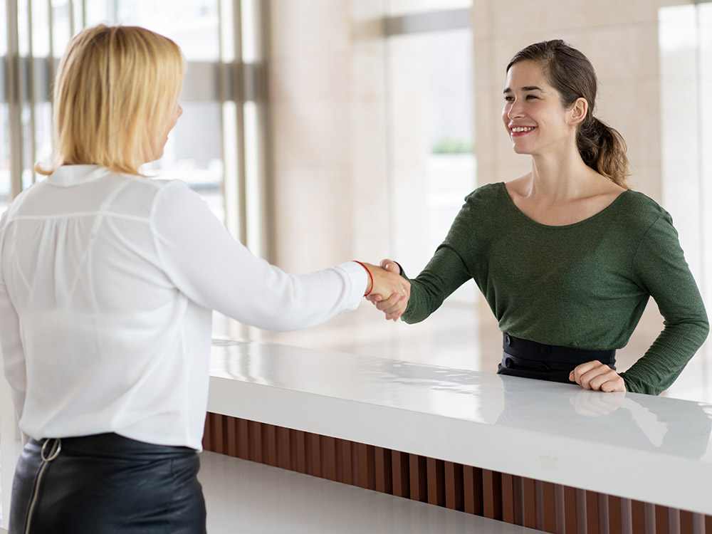 front desk staff and a customer shaking hands (PlatoForms for Hospitality Industry)