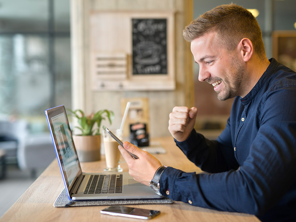 Man smiling in front of his phone and laptop after generating leads through online web forms
